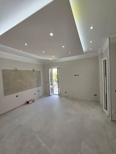 Stanza con controsoffitto bordato di luce, faretti incassati, prese a parete e una lastra appoggiata al muro.