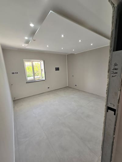 Stanza con finestra, controsoffitto con faretti incassati accesi, placche e prese alle pareti; finiture in corso.