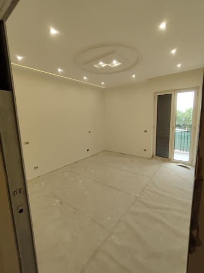 Stanza con faretti incassati, un elemento circolare illuminato al centro del soffitto e una linea di luce in alto sulla parete sinistra.