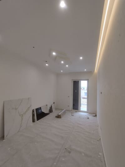 Stanza con una linea luminosa calda lungo l'attacco tra parete e soffitto, faretti incassati e lastre appoggiate alla parete.