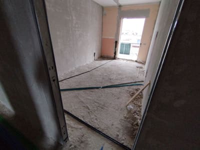 Stanza grezza vista da una porta, con tubi scuri stesi sul pavimento verso una porta finestra.