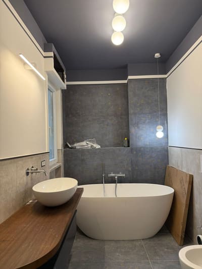 Bagno con soffitto grigio scuro, tre luci a sfera, una lampada lineare a parete e una piccola sospensione; vasca ovale e lavabo da appoggio.