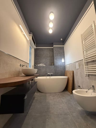 Bagno con luci a sfera sul soffitto scuro, lampada lineare a parete, vasca ovale e scaldasalviette bianco.