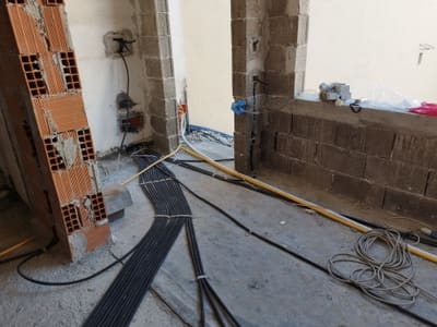 Cantiere grezzo con pareti in mattoni e tufo, fasci di tubi corrugati stesi sul pavimento e scatole di derivazione a muro.