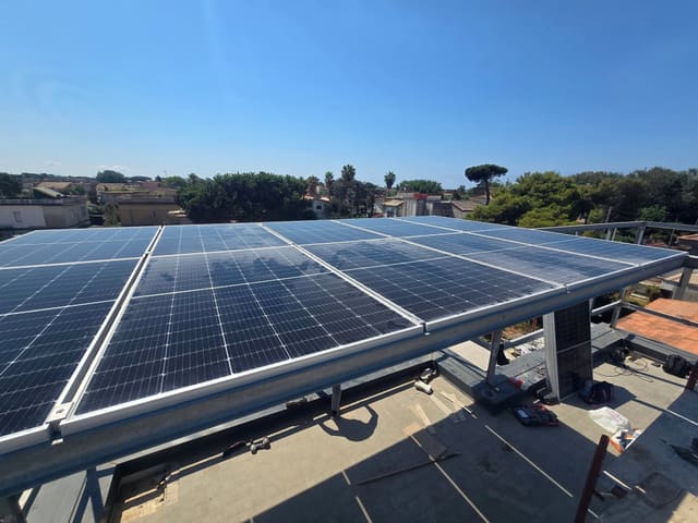 Moduli fotovoltaici montati su una struttura metallica sopra un tetto piano, sotto un cielo sereno.