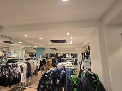 Vista ampia di un reparto di abbigliamento con faretti incassati nel soffitto, un pilastro verde acqua, manichini e stender.