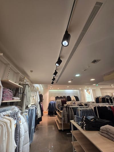 Binario nero con proiettori che corre sul soffitto accanto a scaffali pieni di capi piegati.