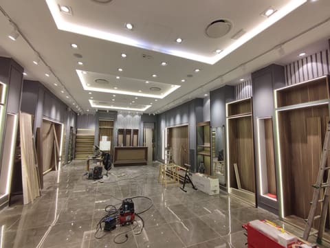 Negozio con controsoffitto a più livelli illuminato da strisce LED nascoste e faretti incassati.