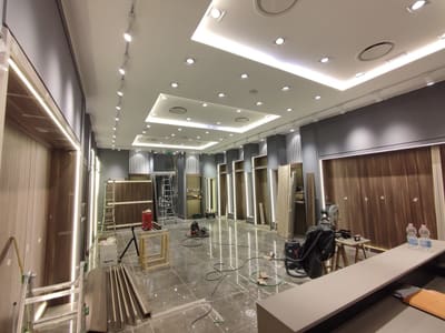 Interno di negozio visto da dietro un bancone grigio: soffitto con gole luminose e faretti, binario con faretti a sinistra, pannelli in legno con cornici luminose.