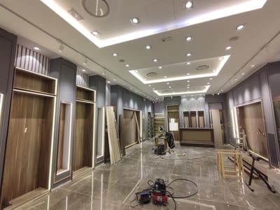 Parete con grandi pannelli in legno scuro contornati da strisce luminose, soffitto con gole LED e faretti, un aspiratore e cavi sul pavimento.