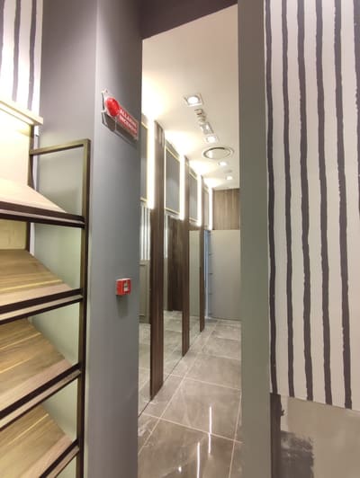 Corridoio stretto con pavimento lucido, mensole in legno a sinistra, parete a righe a destra e faretti accesi nel soffitto.