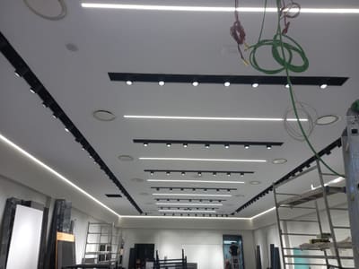 Vista dal basso di binari neri con proiettori e linee LED parallele nel soffitto, con matasse di cavi verdi appese in primo piano.