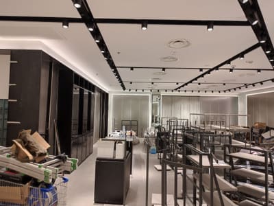 Binari neri che si incrociano sul soffitto sopra un'area piena di espositori metallici e mobili scuri in montaggio.