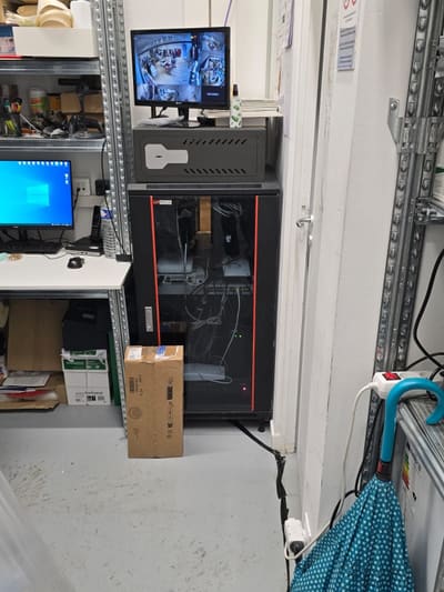 Monitor che mostra le immagini di più telecamere, appoggiato sopra un armadio rack nero, accanto a una scrivania con un computer.