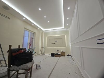 Controsoffitto con gola LED e faretti accesi, parete di fondo con nicchia illuminata e, in primo piano, una sedia con una borsa da lavoro.