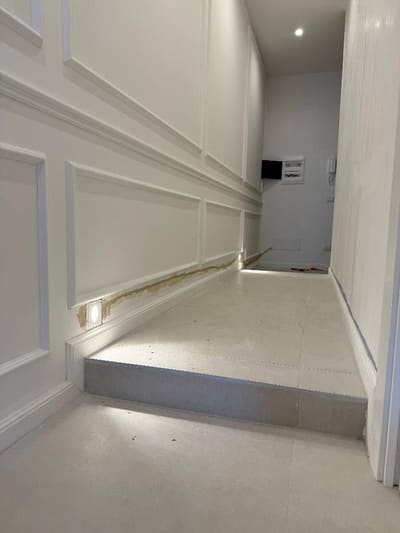 Corridoio con pareti a cornici bianche, un gradino e piccole luci incassate in basso nella parete che illuminano il pavimento.