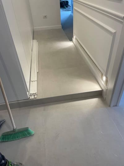 Gradino in un passaggio con una piccola luce incassata nella parete che illumina il pavimento; in primo piano una scopa.