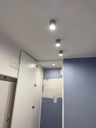 Corridoio con tre faretti cilindrici fissati al soffitto e una parete blu ancora in lavorazione.